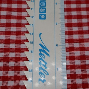 May include: A white ruler with blue markings and the word "Mettler" in blue script. The ruler is placed on top of a red and white gingham fabric.