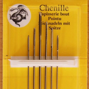 May include: A pack of six John James Chenille needles, size 18/24, displayed on a yellow card. The packaging features the text 6 Needles, JJ18884, Size 18/24, John James, Est. 1840, Chenille, Tapisserie bout Pointu, and Finest Quality Needles.