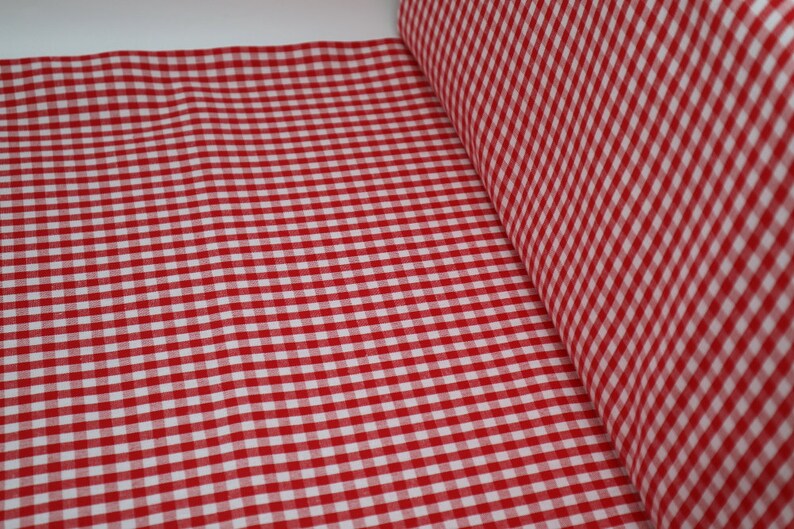 May include: Red and white gingham fabric with a small check pattern. The fabric is folded in half and the edges are visible.