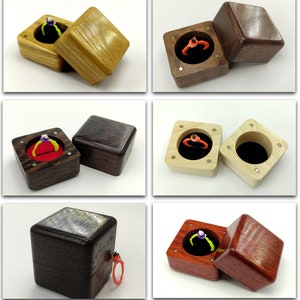 May include: Six different wooden ring boxes with velvet interiors. The boxes are made of various wood types, including walnut, cherry, and maple. The boxes are open and closed, showing the interior and exterior of the boxes.