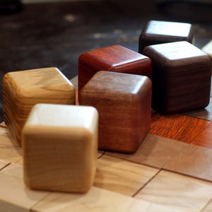 May include: Six wooden blocks of different colors and wood grains. The blocks are arranged in a row on a wooden surface.