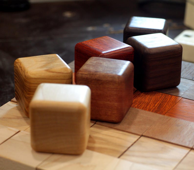 May include: Six wooden blocks of different colors and wood grains. The blocks are arranged in a row on a wooden surface.