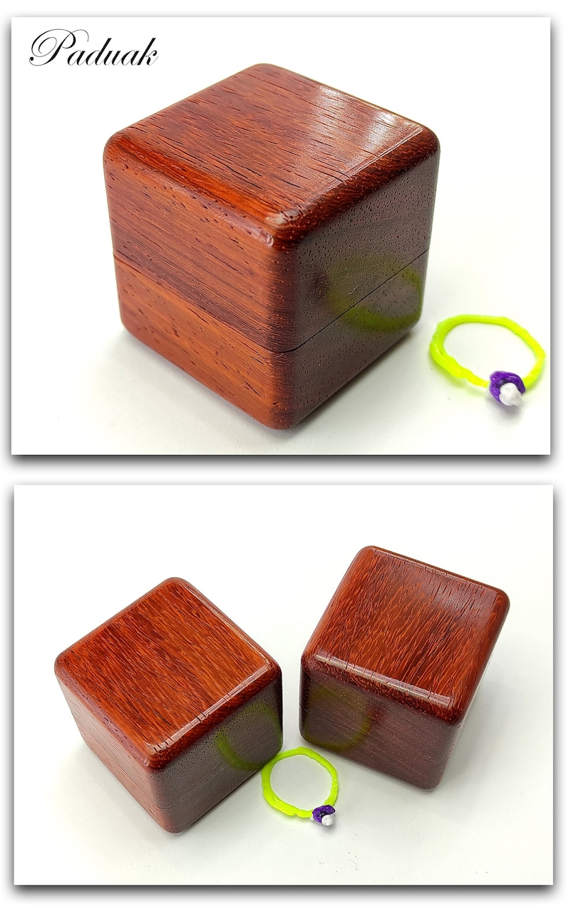 May include: Two small, square wooden boxes made of paduak wood. The boxes are closed and have a rich reddish-brown color. A green rubber band with a purple bead is in front of the boxes.