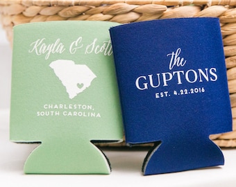 May include: A wicker basket filled with green and blue personalized can coolers. One cooler says "Kayla & Scott" with a heart and the outline of South Carolina. The other cooler says "The Guptons Est. 4.22.2016".