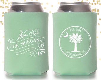 May include: A pair of green can coolers with white text. One cooler says "The Morgans" with a floral design. The other cooler has a circle with a palm tree, crescent moon, and the text "EST. 2016 CHARLESTON, SC".