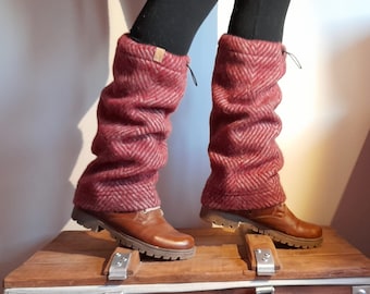 May include: Red and white patterned leg warmers with a black drawstring. The leg warmers are worn over brown boots and are on a wooden surface.