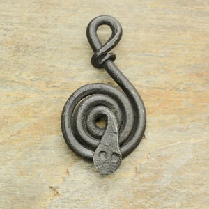 May include: A black metal pendant shaped like a coiled snake with a loop at the top. The snake is curled into a spiral shape with a small head at the bottom.