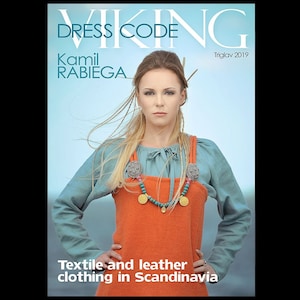 May include: Magazine cover showing a woman in Viking-style clothing. She is wearing an orange wool dress over a blue blouse, with decorative brooches and a turquoise and gold necklace. The magazine title is "VIKING DRESS CODE", with the name "Kamil Rabiega" and the text "Textile and leather clothing in Scandinavia."
