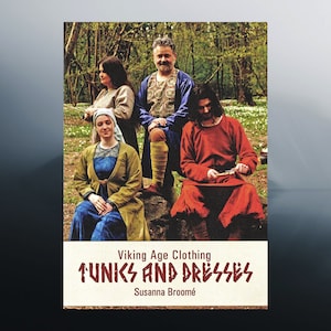 Może przedstawiać: Okładka książki z tytułem "Viking Age Clothing Tunics and Dresses" autorstwa Susanny Broomé. Okładka przedstawia grupę osób ubranych w historyczne stroje wikingów w leśnym otoczeniu.
