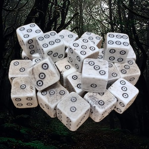 May include: A close-up of a pile of white dice with black dots. The dice are made of bone and have a natural, rustic look. They are arranged in a random pattern, with some dice stacked on top of others.
