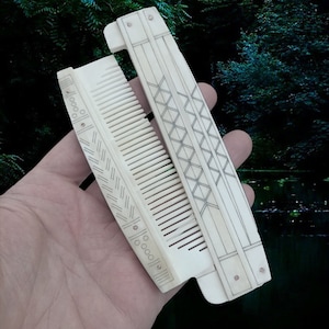 May include: A white folding comb with intricate geometric designs carved into the surface. The comb is made of bone and has a traditional style.