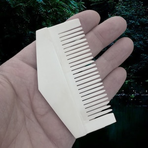 Può includere: Pettine di plastica bianco con forma triangolare e una fila di denti su un lato.