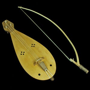 Può includere: Uno strumento musicale in legno con un corpo a forma di pera e un arco. Lo strumento ha una finitura marrone chiaro e una corda che corre lungo la lunghezza del corpo.