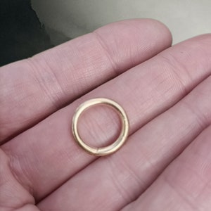 May include: A gold-coloured metal ring, approximately 2.5 cm in diameter, is shown on a person's hand.