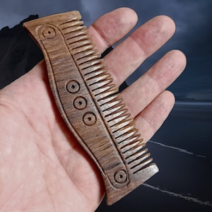 May include: A wooden comb with a curved handle and a row of teeth. The handle has three decorative circles carved into it.