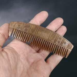 May include: A wooden comb with a carved design. The comb is brown and has a curved shape. The design on the comb is intricate and includes geometric patterns.