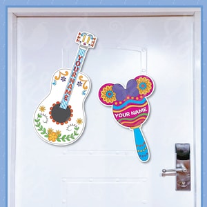 May include: Two decorative cutouts: a white guitar with colorful floral designs and the text "YOUR NAME" and a Mickey Mouse-shaped maraca with the text "YOUR NAME". The guitar and maraca are hanging on a white door.
