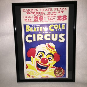 May include: A vintage circus poster advertising Clyde Beatty Cole Bros. Combined Circus. The poster features a smiling clown with red hair and a red nose, against a blue background. The text on the poster reads "Garden State Plaza, Rtes. 4 & 17, Paramus, Tuesday May 26 thru Thursday May 28, Performances 4:30 PM, Clyde Beatty Cole Bros. Combined Circus, The World's Largest Circus."