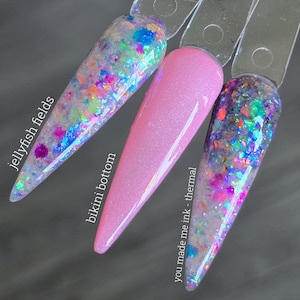 May include: Three nail polish samples on clear sticks. The first is a clear base with colorful glitter and the text "jellyfish fields". The second is a solid pink with the text "bikini bottom". The third is a clear base with glitter and the text "you made me ink - thermal".