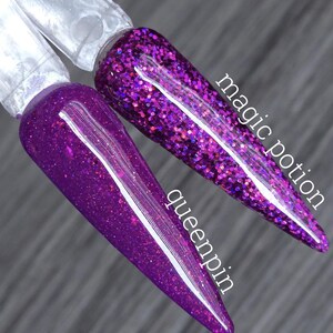 Puede incluir: Dos muestras de esmalte de uñas con purpurina morada. Una está etiquetada como "magic potion" y la otra como "queenpin". El esmalte de uñas es de un morado intenso con un acabado brillante. Las muestras están sobre palitos de plástico transparente.