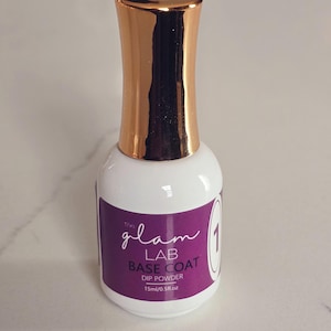May include: A white nail dip powder bottle with a gold cap. The label is purple with the text "the glam LAB BASE COAT DIP POWDER" and the number "1". The bottle contains 15ml/0.5fl oz of product.