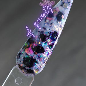 May include: A nail swatch with a glitter design. The glitter is a mix of black, purple, pink, and iridescent colors. The text "of quartz" is written in a purple script over the swatch.