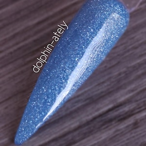 May include: A blue nail polish sample with a glittery finish. The sample is on a clear stick, showcasing the color and texture. The text "dolphin-ately" is printed on the sample.