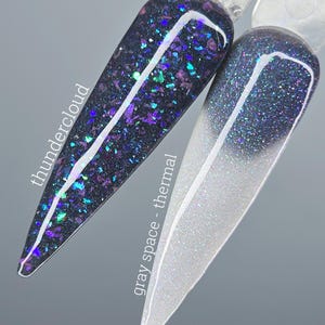 Könnte beinhalten: Zwei Nagellack-Swatches. Einer ist dunkel mit lila und türkis Glitzer, beschriftet mit "thundercloud". Der andere ist ein Farbverlauf von Weiß zu Grau mit Glitzer, beschriftet mit "gray space - thermal".
