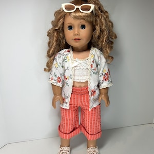 May include: A doll wearing a white floral print jacket, a white lace top, and coral striped capri pants. The doll has curly blonde hair, white sunglasses, and crochet sandals. The outfit is a summer-themed ensemble.