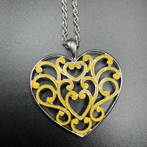 May include: Silver-toned heart pendant necklace with a yellow filigree design. The pendant is heart-shaped with an openwork design filled with yellow enamel. The necklace has a silver chain.