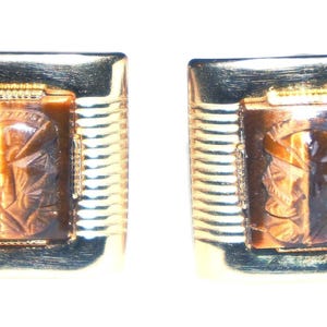 May include: A pair of gold cufflinks with tiger's eye stone insets. The stones are carved with a design.