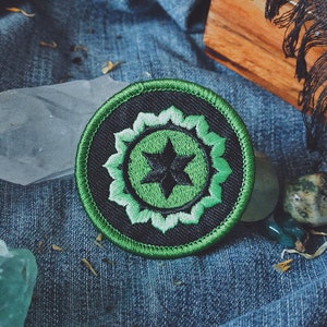 Peut inclure: Un patch brodé vert et noir avec une étoile à cinq branches au centre. L'étoile est entourée d'un cercle vert avec un contour blanc. Le cercle est entouré d'un cercle noir avec un contour vert.