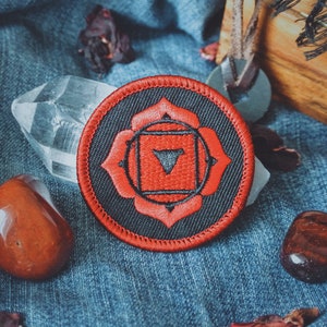 May include: A red and black embroidered patch with a stylized flower design and a triangle inside. The patch is on a blue denim background.