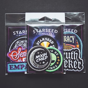 Puede incluir: Tres bolsas de plástico transparentes con varios parches bordados. Los parches presentan frases como "Sense of Freedom", "Empathy", "Moon Child", "Truth Seeker" y "Is Be Ends".