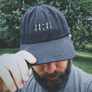 Könnte beinhalten: Eine schwarze Baseballkappe mit einem weißen gestickten Design der Zahlen "11:11".