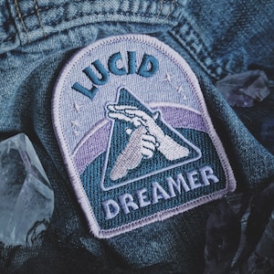 May include: A blue and purple embroidered patch with the text "LUCID DREAMER" and a hand gesture in the center.
