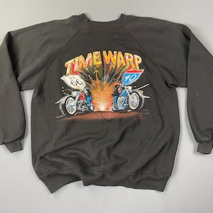 May include: A black sweatshirt with a graphic print of two motorcycles speeding down a road with the text "TIME WARP" above them. The motorcycles have US Route 66 and 70 signs attached to them.