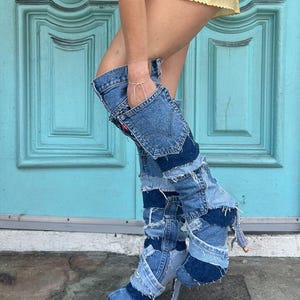 May include: Denim patchwork knee-high boots in various shades of blue. The boots feature a stiletto heel and are constructed from repurposed denim. The design includes pockets and seams, creating a unique, upcycled fashion statement. The boots are worn with a yellow satin mini skirt.