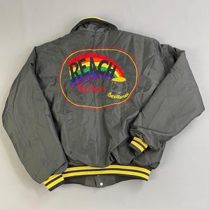 May include: Black satin bomber jacket with yellow and black striped cuffs and waistband. The back of the jacket features a large embroidered patch with a rainbow, the words "REACH" and "Big Dream Excellence".