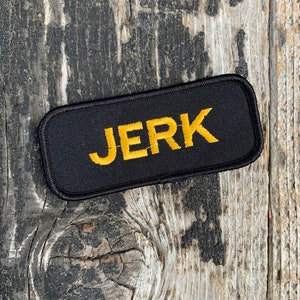 May include: Black patch with the word "JERK" embroidered in yellow thread.