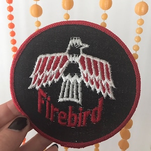 May include: A black and red embroidered patch with a white bird and the word "Firebird" in red lettering.