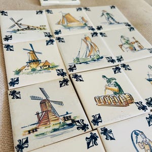 May include: A collection of square ceramic tiles featuring hand-painted illustrations in blue, brown, and green. Each tile displays scenes of windmills, sailing ships, and figures performing tasks, accented with dark blue fleur-de-lis corner motifs.