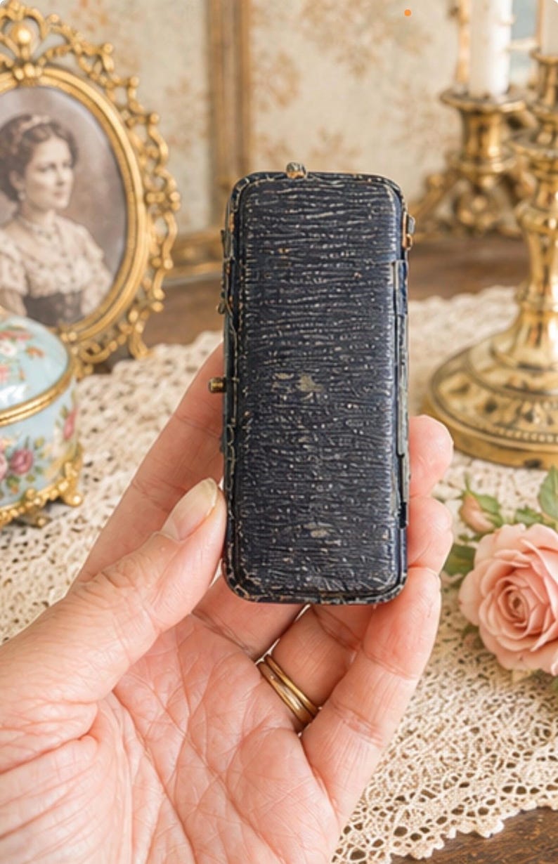 May include: A rectangular, dark navy blue jewellery box with a textured, pebbled exterior finish. The small, elongated case features visible metal hinges along the side and a worn, aged appearance with slight scuffing on the edges and surface.