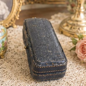 May include: A rectangular, dark blue, textured jewellery box with a hinged lid. The exterior features a subtle, embossed pattern across the top and sides, accented by fine, light-coloured stitching along the edges and a small, metallic latch closure.