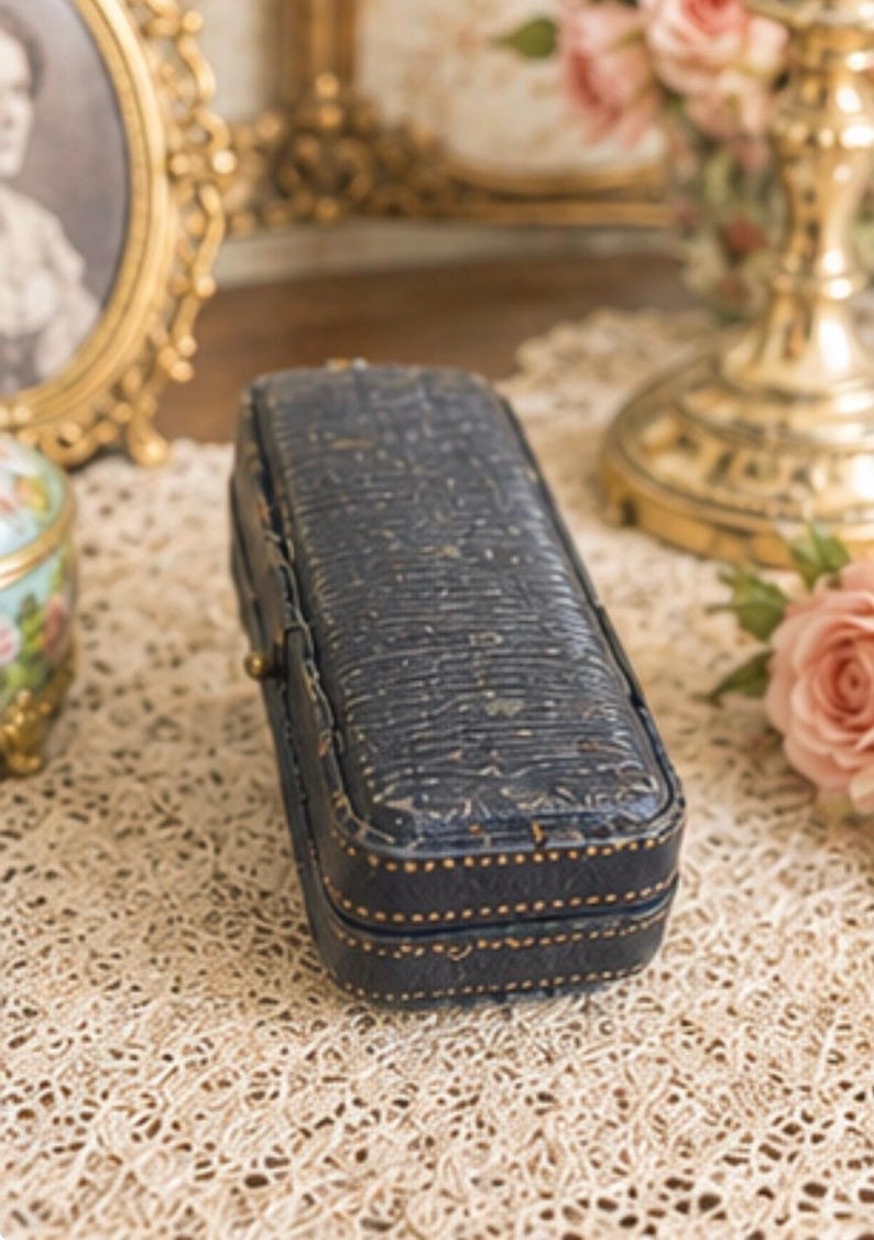 May include: A rectangular, dark blue, textured jewellery box with a hinged lid. The exterior features a subtle, embossed pattern across the top and sides, accented by fine, light-coloured stitching along the edges and a small, metallic latch closure.