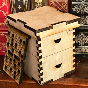 May include: A wooden box with two drawers and a honeycomb design on the side. The box is made of light wood with dark brown trim. The box is sitting on a wooden surface.