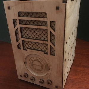 May include: A wooden box with a decorative front panel featuring a woven pattern and a circular design. The box has four knobs on the bottom.