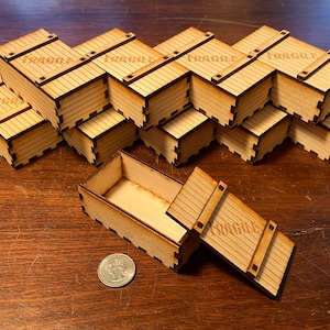 May include: A stack of 10 small wooden boxes with the word "FRAGILE" printed on each box. The boxes are stacked in a staggered pattern. One box is open and the lid is lying next to it. A US quarter is in the foreground for scale.