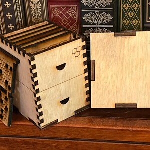 May include: A wooden box with two drawers and a honeycomb design on the front. The box is open and the lid is lying next to it. The box is made of light wood with dark brown accents.
