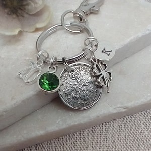 May include: A silver keyring with a sixpence coin, a green crystal charm, a silver charm with the number 50, a silver clover charm, and a silver charm with the letter K.